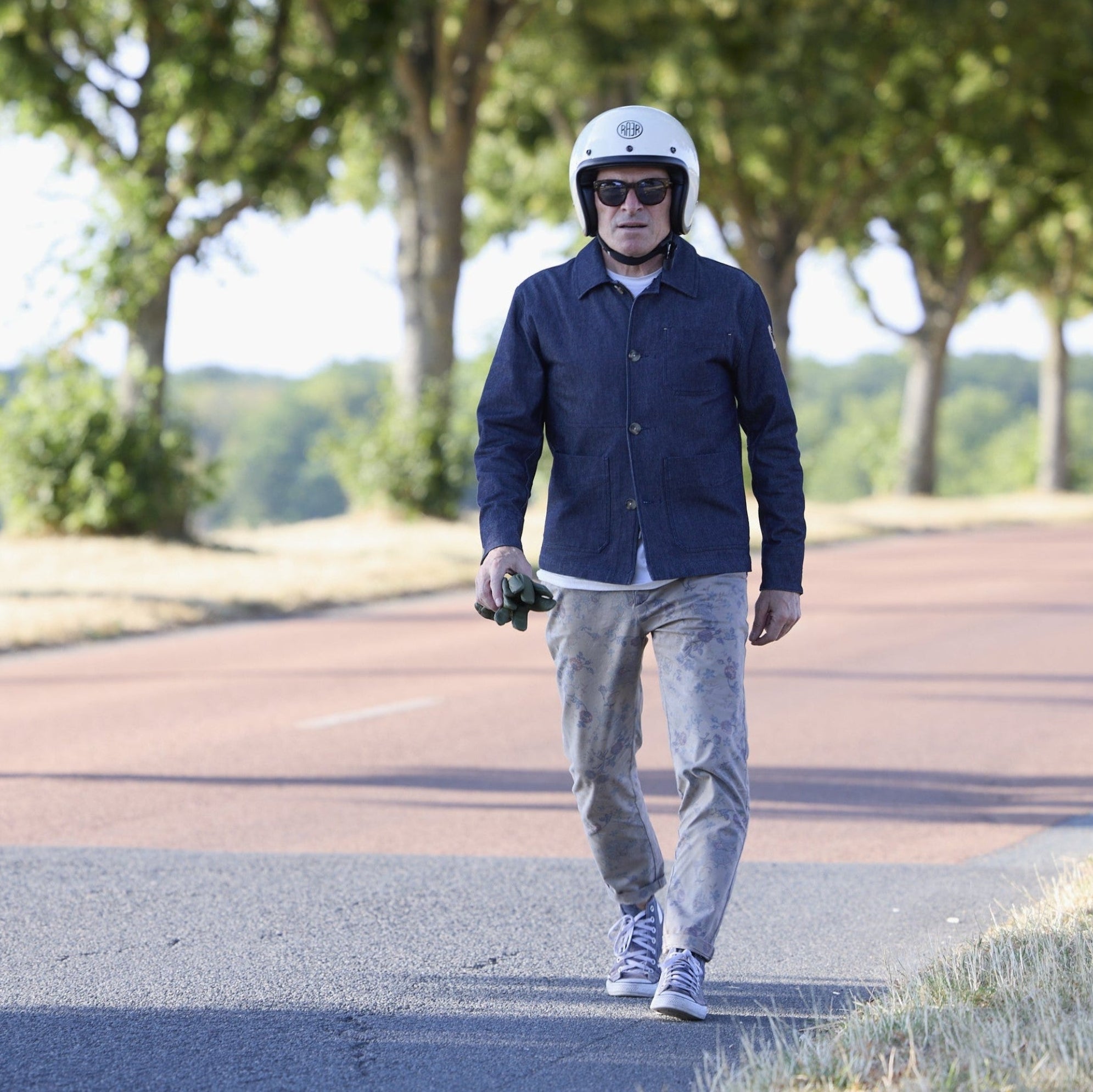 Homme en veste RAER marchant sur une route bordée d’arbres