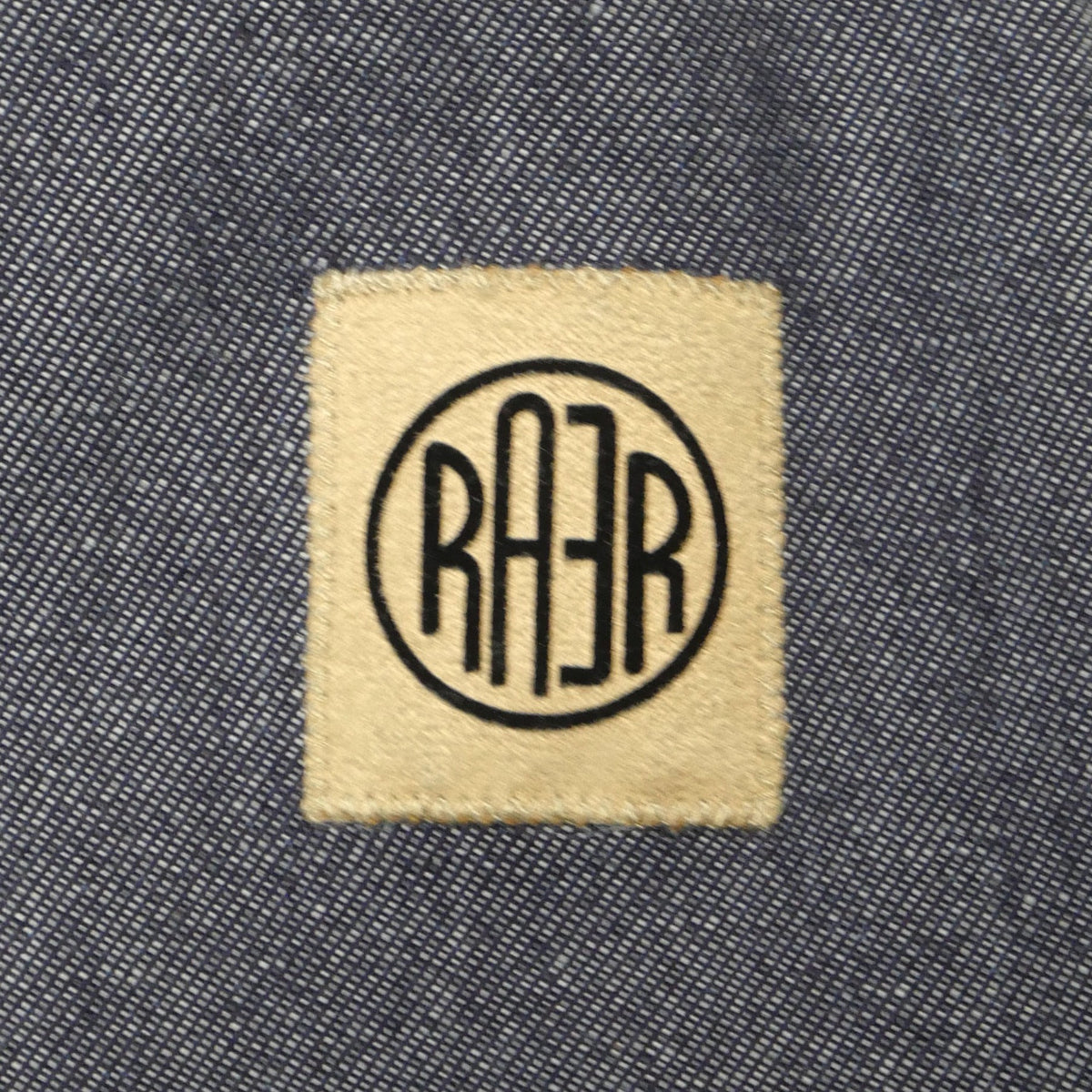 Gros plan du logo RAER cousu sur le denim de la veste ARTIST.