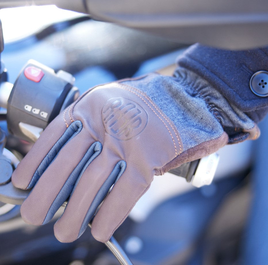 Gant ALAMO porté près du guidon d’une moto, avec cuir marron, dessus en denim et logo RAER.
