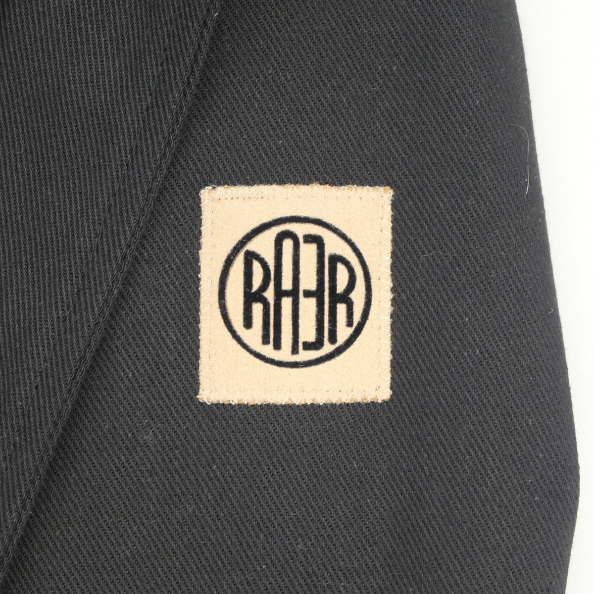 Gros plan du logo RAER cousu sur la toile noire de la veste ARTIST.