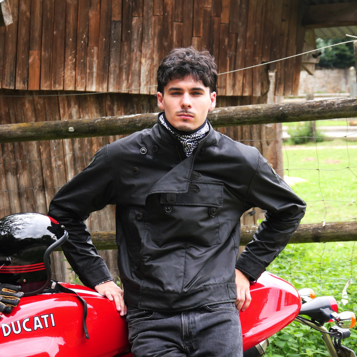 Veste ASCONA 2 WX noire portée de face, devant une moto rouge.