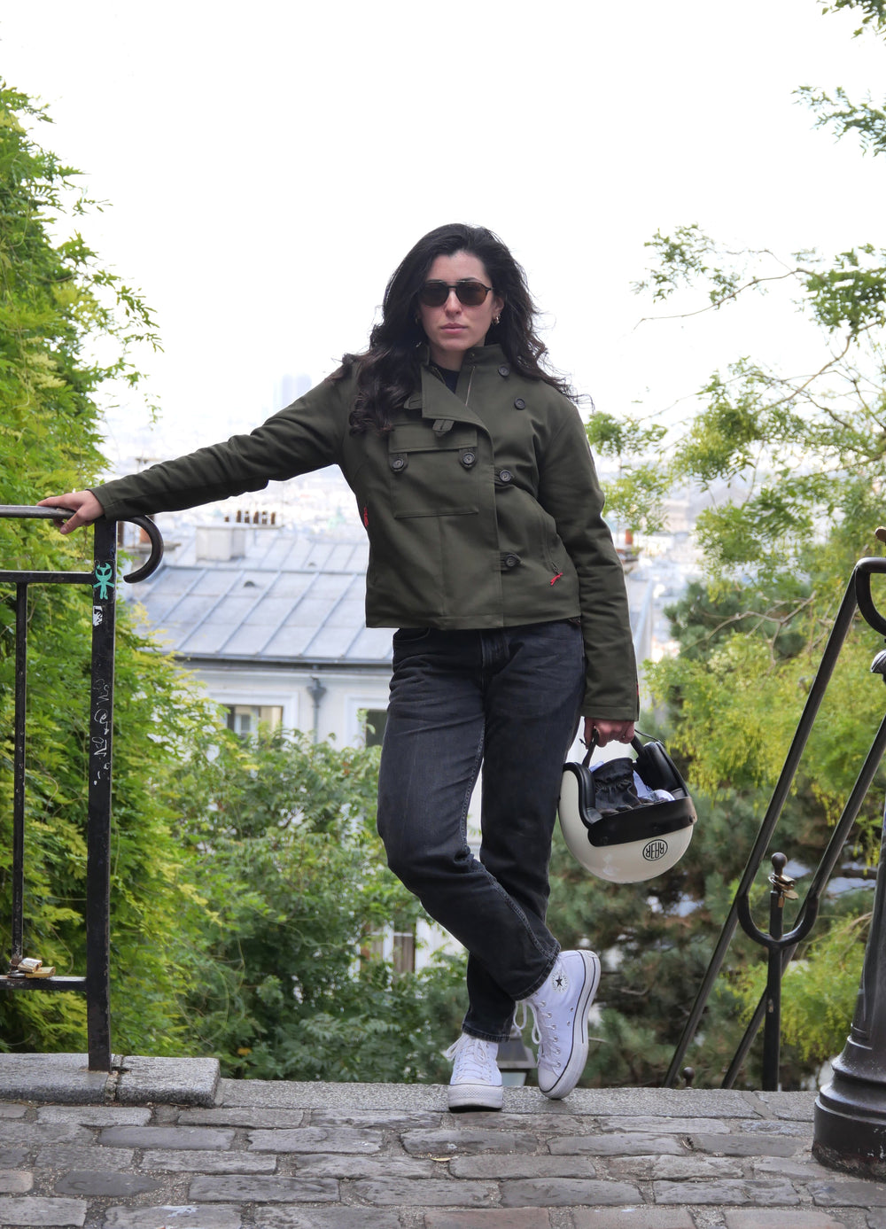 Veste DONNA Armalith kaki portée debout dans un escalier, un casque blanc à la main.