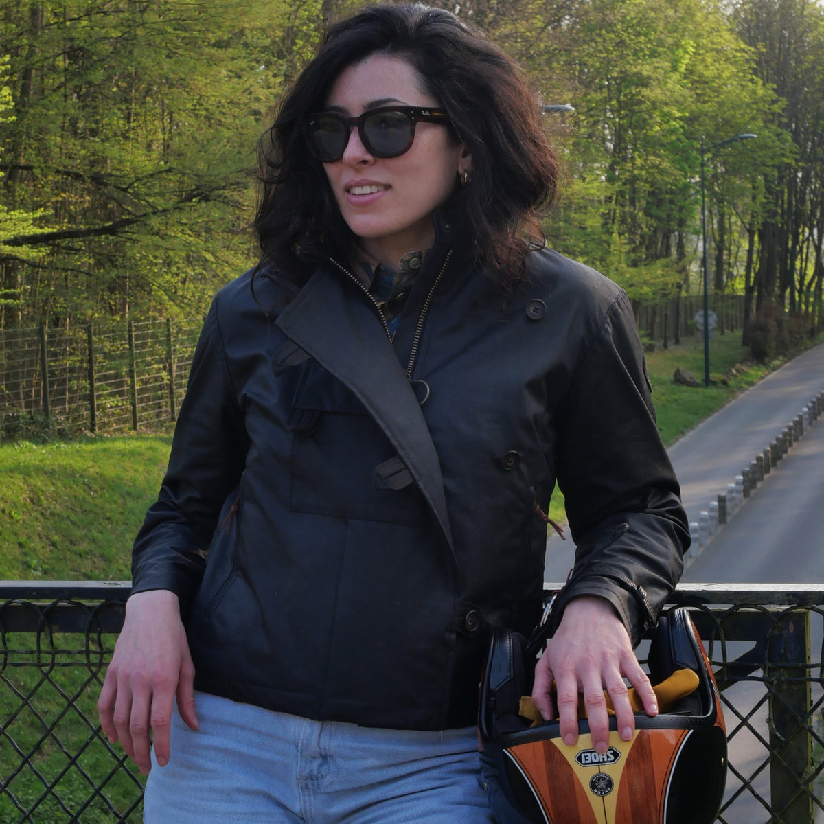 Veste DONNA Wax noire portée de face en extérieur, un casque à la main.