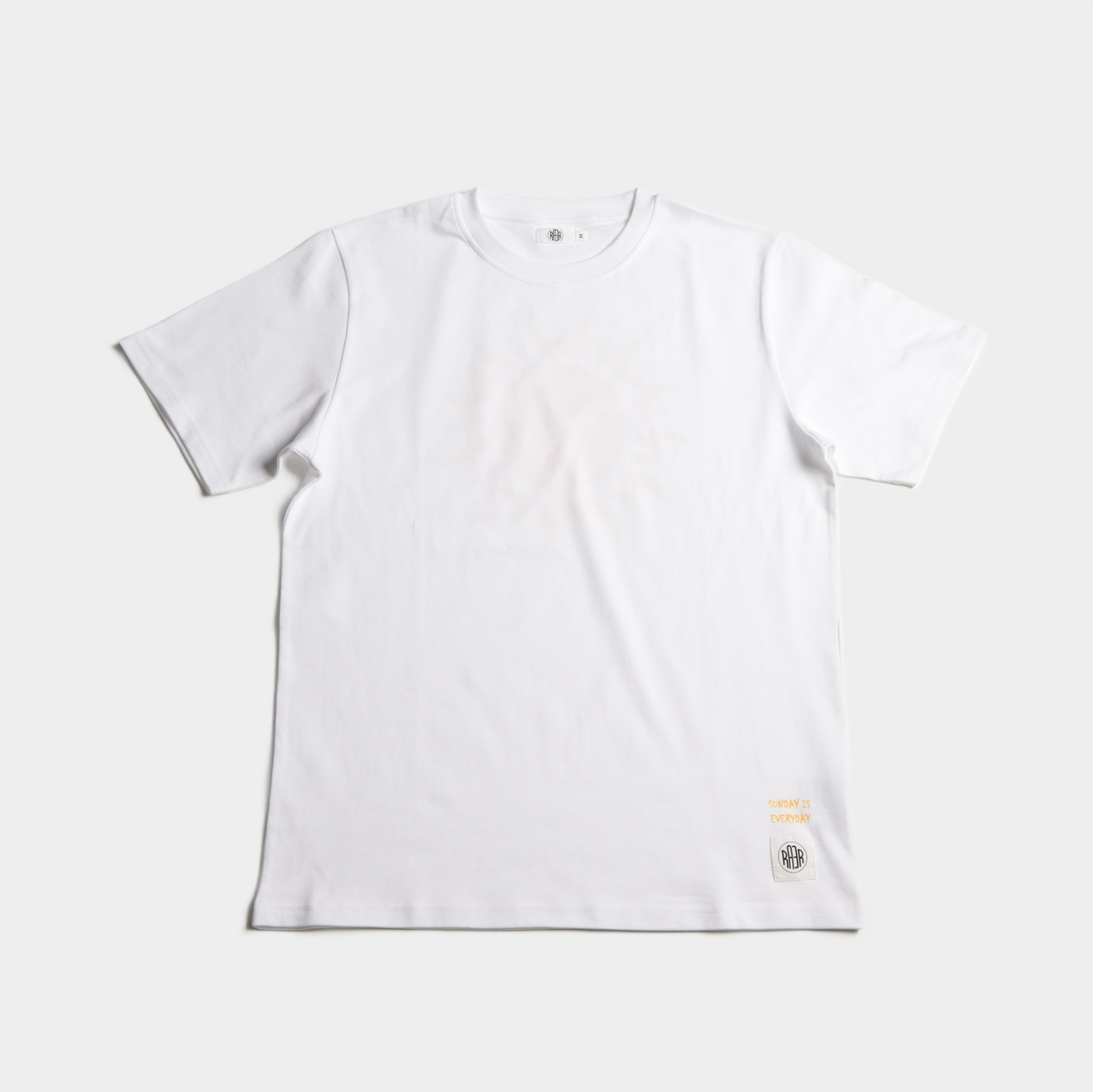 Tee-shirt SUNDAY blanc posé à plat de face, avec petit motif près de l’ourlet.