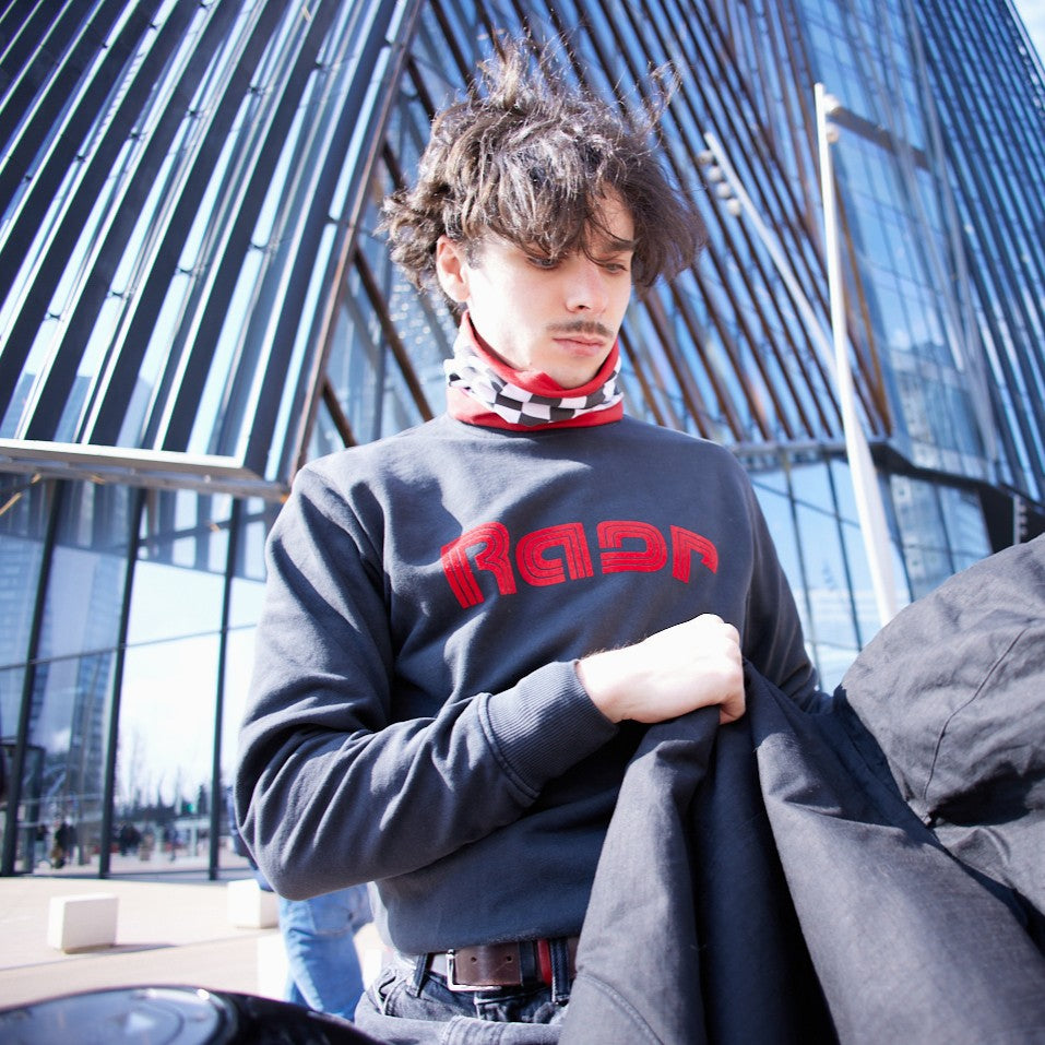 Sweat SPEED noir à logo rouge porté en extérieur par un homme tenant une veste.